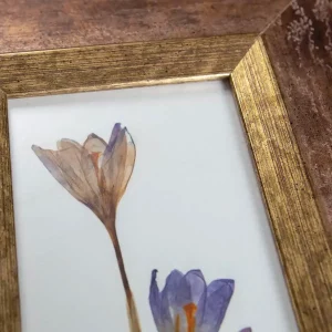 Primer plano de la moldura dorada y cobriza junto a la flor prensada.
